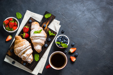 Croissant with fresh berries and cup of coffee on black.