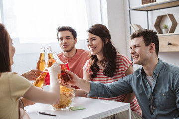 happy friends clinking with bottles and cups while playing name game at home
