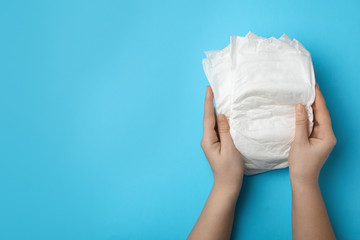 Woman with diapers on light blue background, closeup. Space for text
