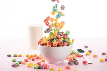 selective focus of bright multicolored breakfast cereal falling in bowl near milk and spoon on...