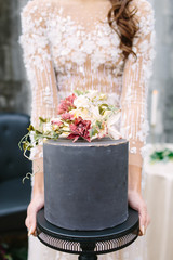 bride holding elegant black wedding cake in white dress