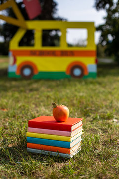 vertical photo of a stack of books with an apple on the background of a school bus layout