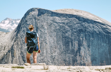 Vrouw wandelaar met blauwe rugzak kijkend naar halve koepelbergen in Yosemite National Park vanuit de noordelijke koepel