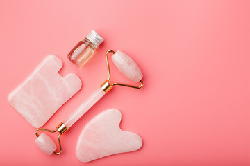 A set of tools for face Massage technique Gua Sha made of natural rose quartz on a pink background. Roller, jade stone and oil in a glass jar for face and body care.