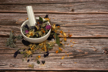 Phytotherapy. Composition of dry herbs for herbal medicine. A mixture of various medicinal herbs in a porcelain mortar with a pestle on a wooden background. Free space.