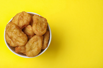 Bucket with tasty chicken nuggets on yellow background, top view. Space for text