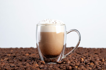  a transparent cup of latte with cinnamon on a foam with a double bottom stands among coffee beans on a white background. Copyspace