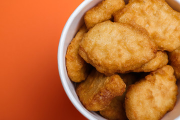 Bucket with delicious chicken nuggets on orange background, top view