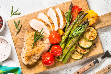 Chicken breast grilled with vegetables on a wooden serving board.