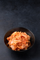 Kimchi cabbage in a black ceramic bowl on a black background. Place for text, top view. Korean food