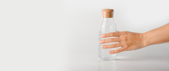 A hand takes a glass bottle filled with clear water on a white background.