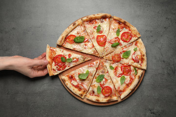Woman taking slice of delicious pizza Margherita at grey table, closeup