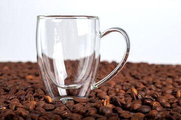 An empty transparent double-bottomed cup stands among coffee beans on a white background. Copyspace