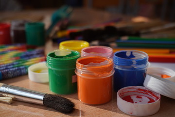 olorful gouache paints in jars. Brushes, paints, pencils for drawing, The concept of the creative workshop of the artist