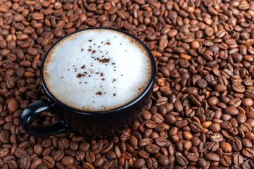 A black cup of black coffee with white froth is on the table where coffee beans are scattered. top shot copyspace