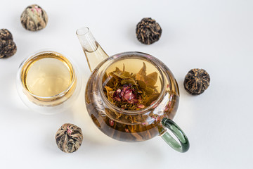 Blooming green tea in a glass teapot. On a light surface. Nearby are tea briquettes of leaves and flowers.