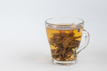 Blooming green tea in a glass teapot. On a light surface. Nearby are tea briquettes of leaves and flowers.