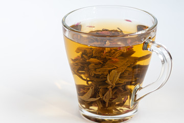 Blooming green tea in a glass teapot. On a light surface. Nearby are tea briquettes of leaves and flowers.