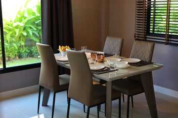 dish ware sets arrange on dining table inside eating room of modern home interior with green garden outside view the window