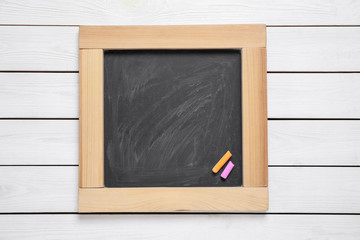 Blackboard with pieces of color chalk on white wooden background, top view. Space for text