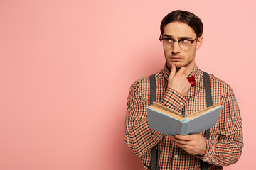 thoughtful male nerd in eyeglasses reading book on pink