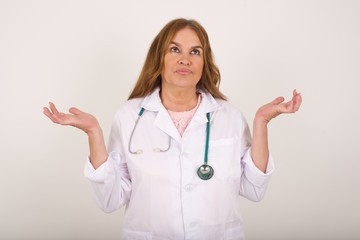 Beautiful doctor woman doubt expression, confuse and wonder concept, uncertain future shrugging shoulders, standing against gray Wall.