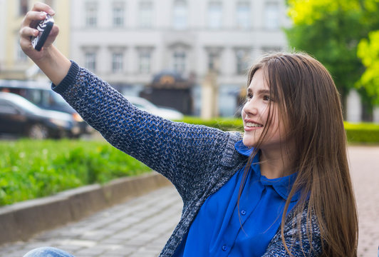A beautiful young girl makes a selfie in the park in good weather for a walk.