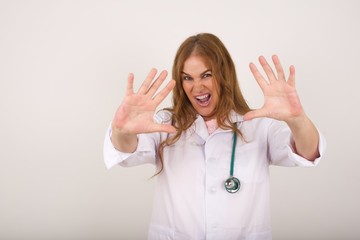 Dissatisfied doctor female model frowns face, has disgusting expression, shows tongue, expresses...