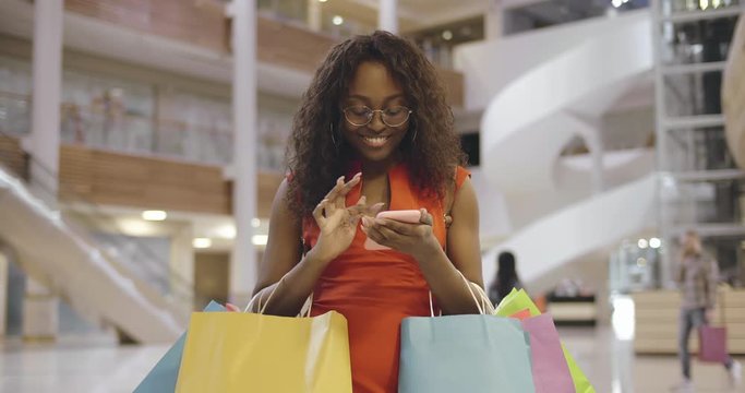 Young african woman with shopping bags using mobile phone in mall