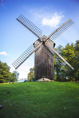 Fototapeta na wymiar Traditional windmill wooden house on a green grass and under a clear blue sky