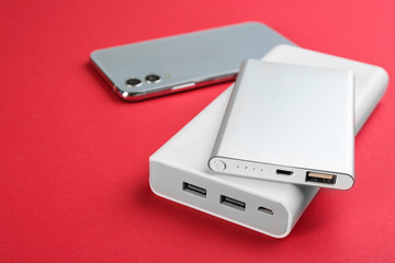 Mobile phone and portable chargers on red background, closeup