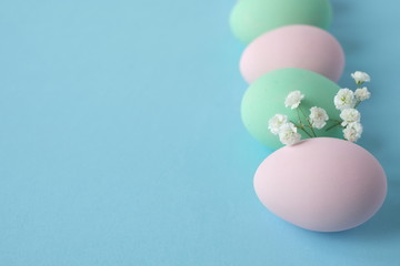 Naklejka na ściany i meble Beautiful easter table setting composition. A row of pastel colored eggs, pink, mint, white gypsophila wildflower flower on blue background. Happy Easter greeting card. Top view