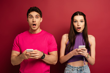 beautiful shocked couple using smartphones on red