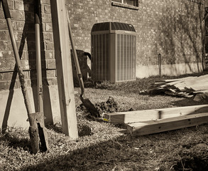 Building new fence.  Backyard with modern air conditioner, shovels and lumber for new privacy fence. Black and white.