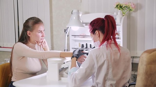 Woman manicurist with gloves in a beauty salon does a hardware manicure to a client before applying a gel coating