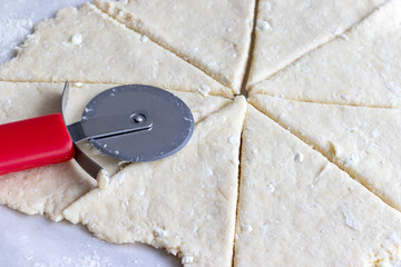 Rolled raw curd dough cut into eight triangles with a red round pizza knife on it on baking paper. The process of making curd bagels or croissants. Closeup view