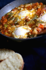 Shakshuka in a pan, with seasonal vegetables and eggs, and two slices of bread. Selective focus.