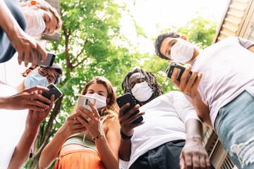 Group of young people of different ethnicities standing together with a mobile phone in hand wearing protective masks