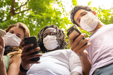 Fototapeta premium Three people of different ethnicities standing together with a mobile phone in hand wearing protective masks