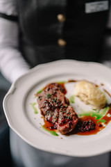 Waitress holding beef steak with potatoes gratin and green sauce on a plate