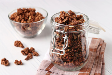 Chocolate Granola crispy muesli with natural honey and nuts in a glass jar and bowl against a white background, healthy food, Horizontal format