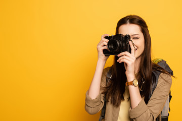 attractive female tourist with backpack holding photo camera on yellow
