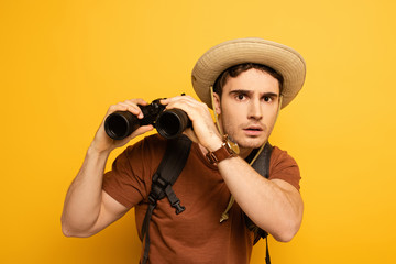surprised traveler in hat with backpack holding binoculars on yellow