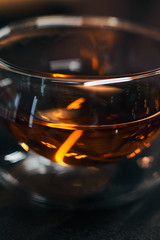 Transparent bowl with black tea on a wooden table. Bright flare of light in the drink.