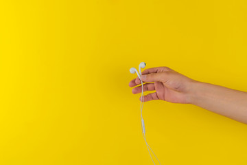 person's hand holding portable wired earphones or headphones isolated against the colorful background, minimalism style, listen to the music