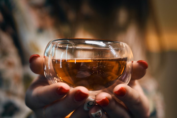Girl's hands hold a transparent cup with black tea. Bright highlights on a glass