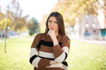 Portrait of thoughtful smiling girl keeps hand under chin, looks directly at camera, listens something with interest, dressed casually, poses against gray wall. Youth concept.