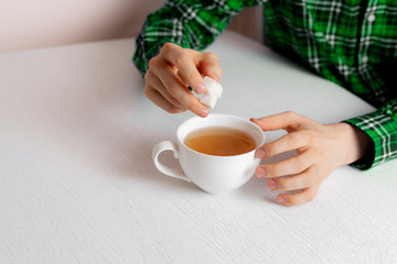 person hand holding some sugar cubes and put them into cup of tea sitting at the table