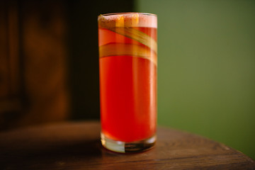 rhubarb sour cocktail in a highball glass on a wooden table, green backround