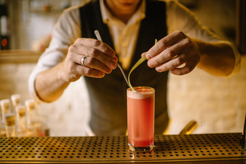 barmen preparing rhubarb cocktail in highball glass and holding slice of rhubarb garnish